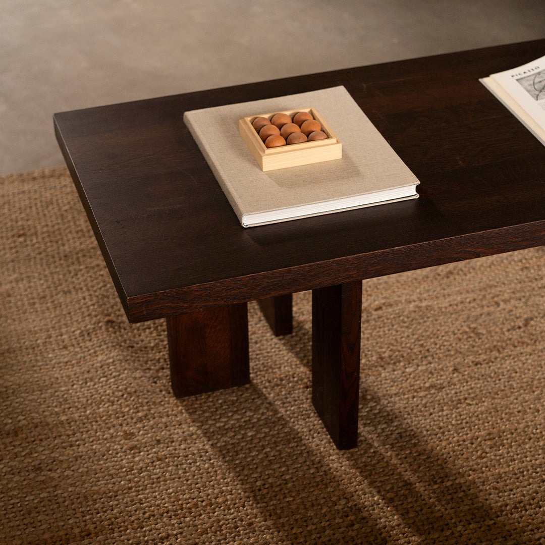 Dark wood coffee table with a smooth surface and clean lines, set on a textured natural fiber rug.