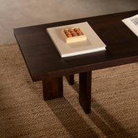 Dark wood coffee table with a smooth surface and clean lines, set on a textured natural fiber rug.