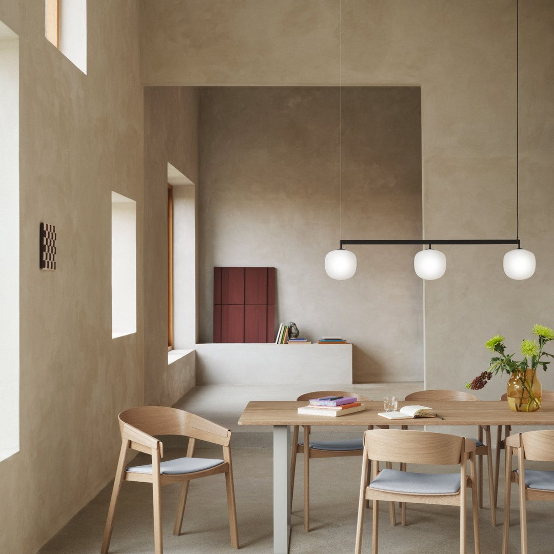 Elegant wooden dining set with soft blue accents, featuring a minimalist gray wall and round white pendant lights.