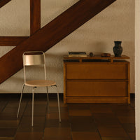 Minimalist chair with a natural wood seat and chrome legs, set against a warm-toned wooden background and textured walls.
