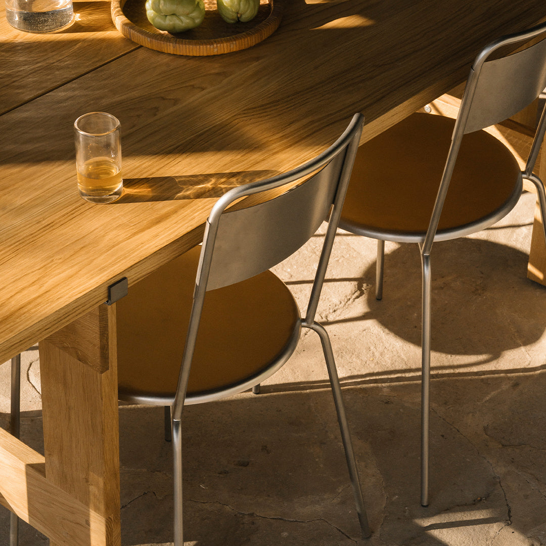 Stylish silver chairs with warm mustard seats, set against a natural wood dining table in a sunlit setting.