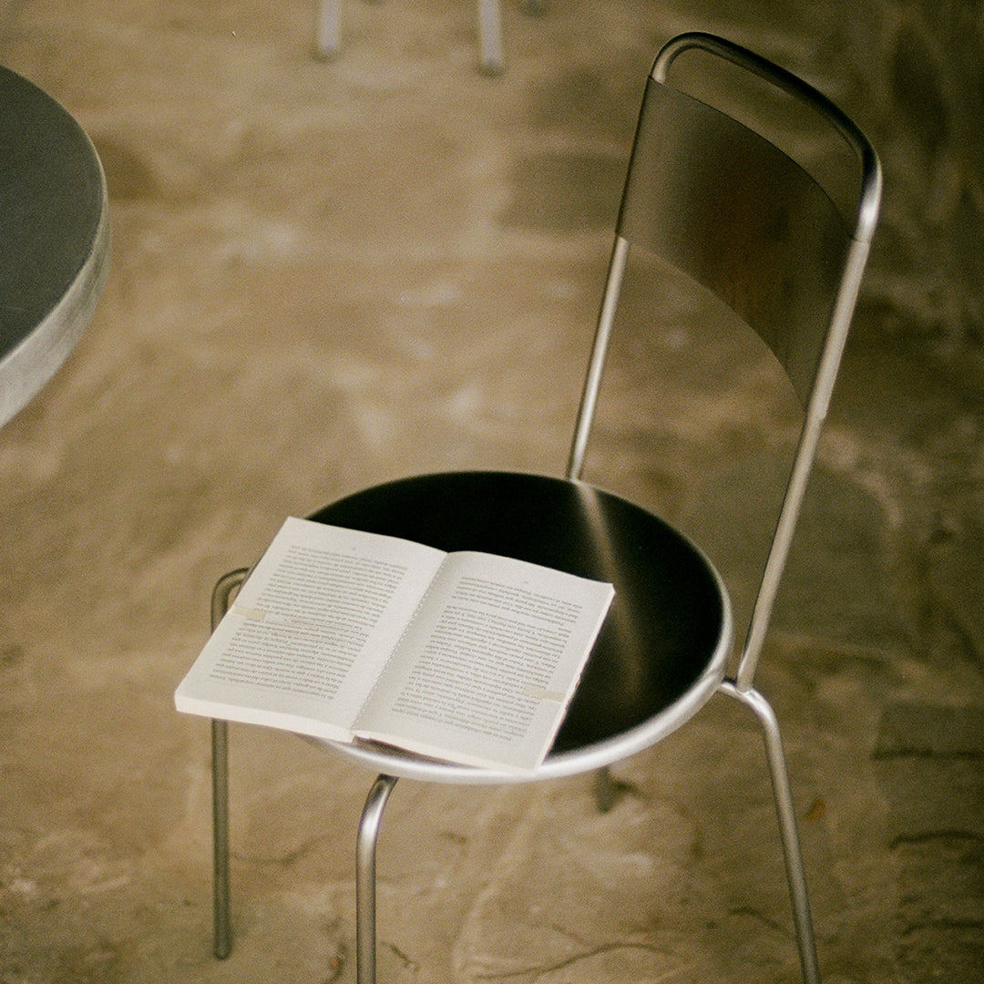 Sleek silver metal chair with a round black seat; features a minimalist design perfect for modern decor.
