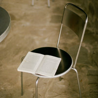 Sleek silver metal chair with a round black seat; features a minimalist design perfect for modern decor.