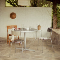 "Modern silver metal table with neutral-toned chairs in a rustic outdoor setting, earthy stone floor and soft natural colors."