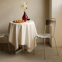 "Elegant cream tablecloth drapes over round table, paired with a striped black and white chair in a minimalist setting."