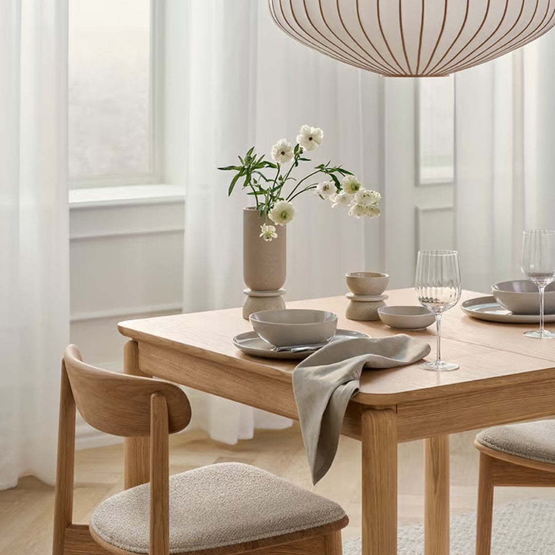 Light wood dining table with neutral tones, soft gray textiles, and a minimalist floral centerpiece. Elegant, modern decor.