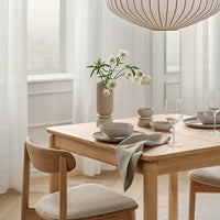 Light wood dining table with neutral tones, soft gray textiles, and a minimalist floral centerpiece. Elegant, modern decor.