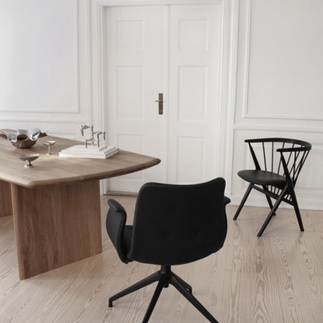 Minimalist black chair and wooden table against a light wall, featuring neutral tones and clean, modern lines.