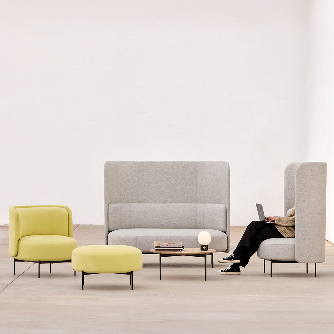 Modern gray upholstered sofa with vibrant yellow accent chairs and ottoman in a minimalist setting.