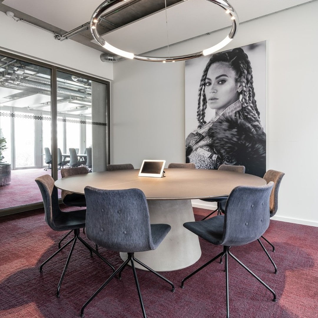 Modern workspace featuring a round wooden table, gray chairs, and a patterned burgundy carpet. Elegant lighting.