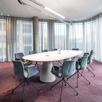 Modern round table with a white surface, surrounded by grey upholstered chairs on a textured burgundy carpet.