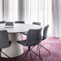 Gray chairs with a sleek design around a round white table, set on rich burgundy carpet in a bright, airy setting.