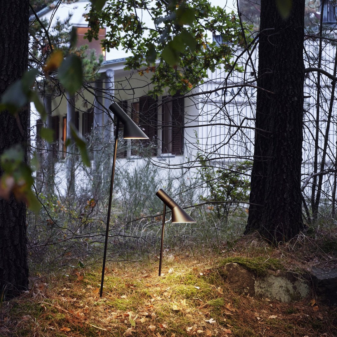 Sleek black outdoor lamps set against a backdrop of green foliage and a rustic white cabin. Soft natural lighting.