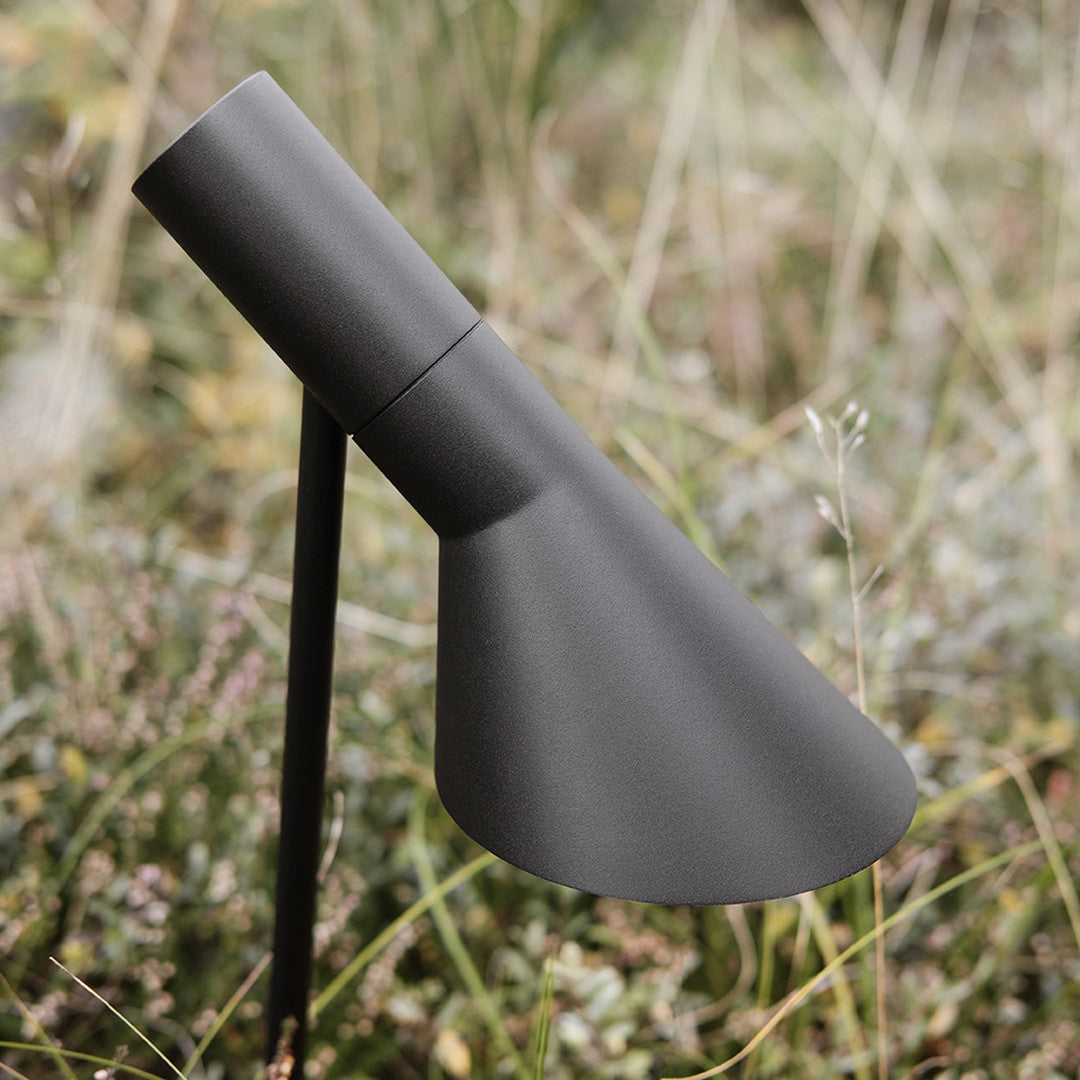 Sleek matte black outdoor light fixture with a modern conical design, set against a natural grass background.