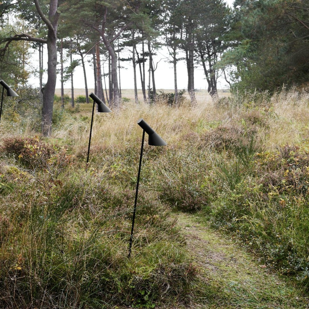 Black outdoor lamps on slender poles amidst lush green grass and wildflowers, set in a natural, serene landscape.