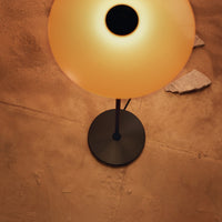Modern lamp featuring a matte black base and a warm, glowing amber shade against a textured beige surface.