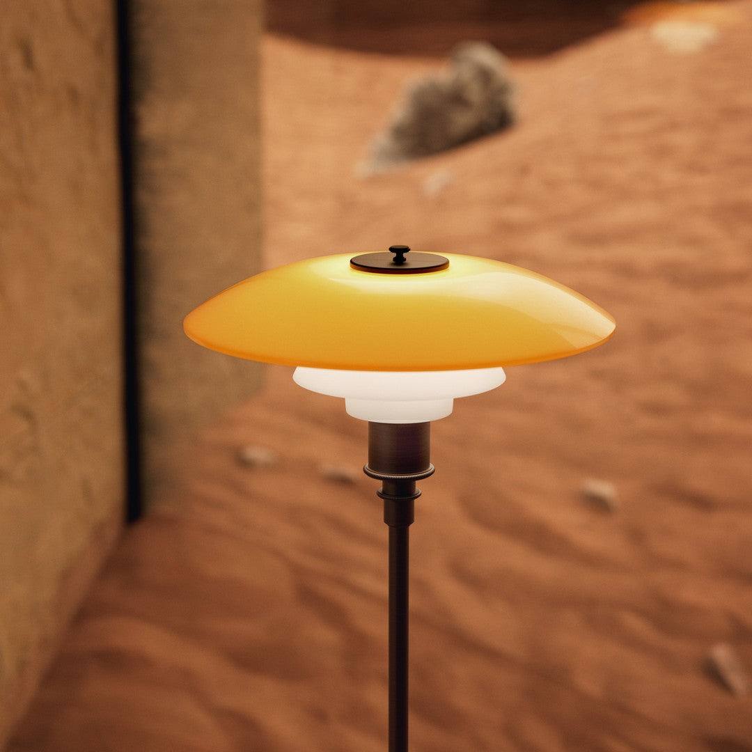 Stylish lamp with a smooth yellow and white glass shade, set against a sandy, rustic background.