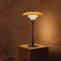 "Modern table lamp featuring a layered design with orange, white, and black elements against a warm, textured wall."