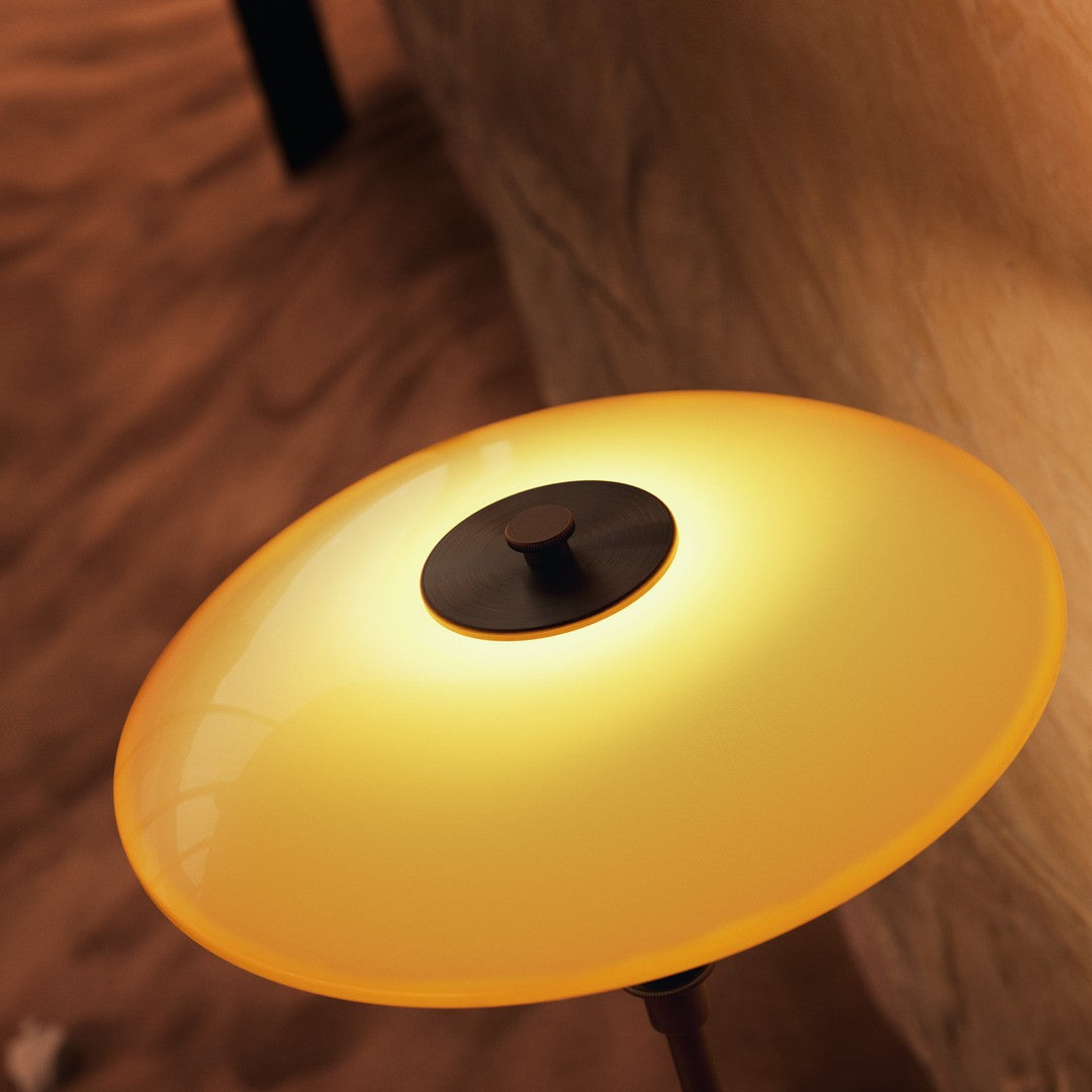 Round, glossy lamp shade in warm yellow with a sleek black center, set against a subtle textured background.