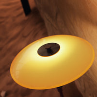 Round, glossy lamp shade in warm yellow with a sleek black center, set against a subtle textured background.