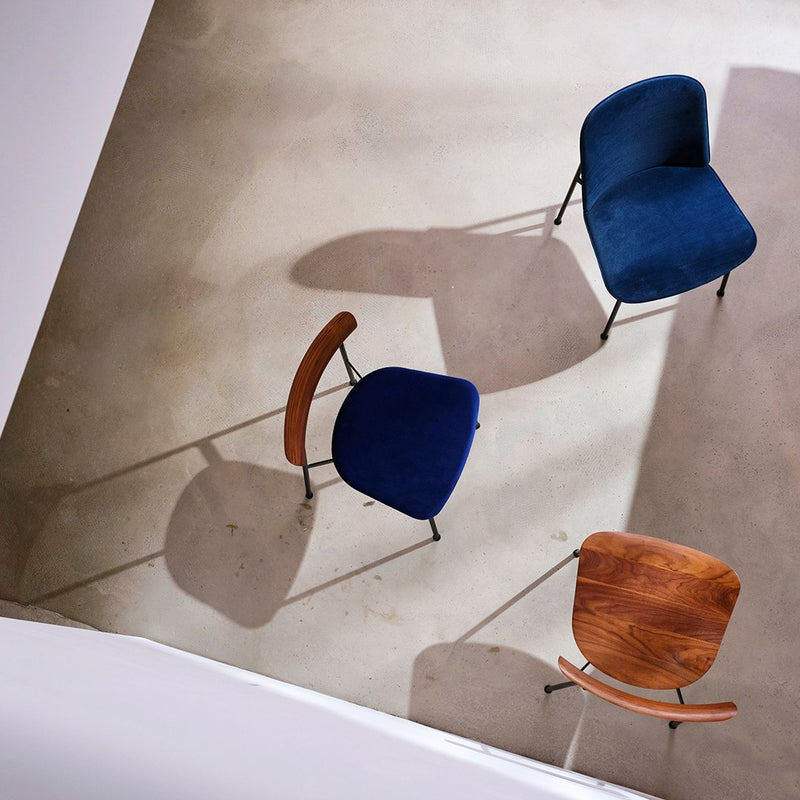 Mid-century modern chairs in navy blue and walnut wood with soft shadows on a light concrete floor.