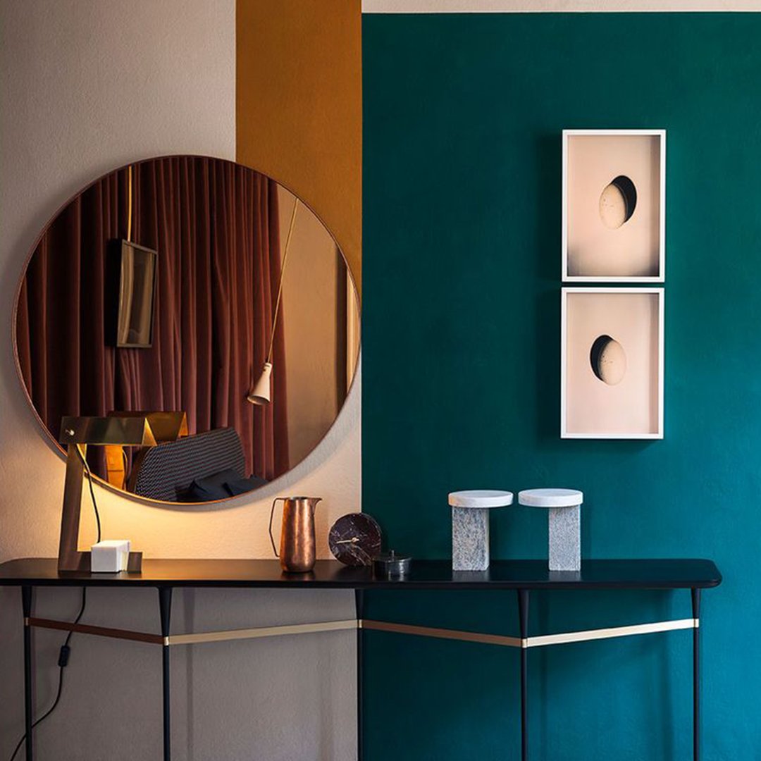 Elegant teal and gold wall design featuring a round mirror and minimalist art prints on a sleek black table.
