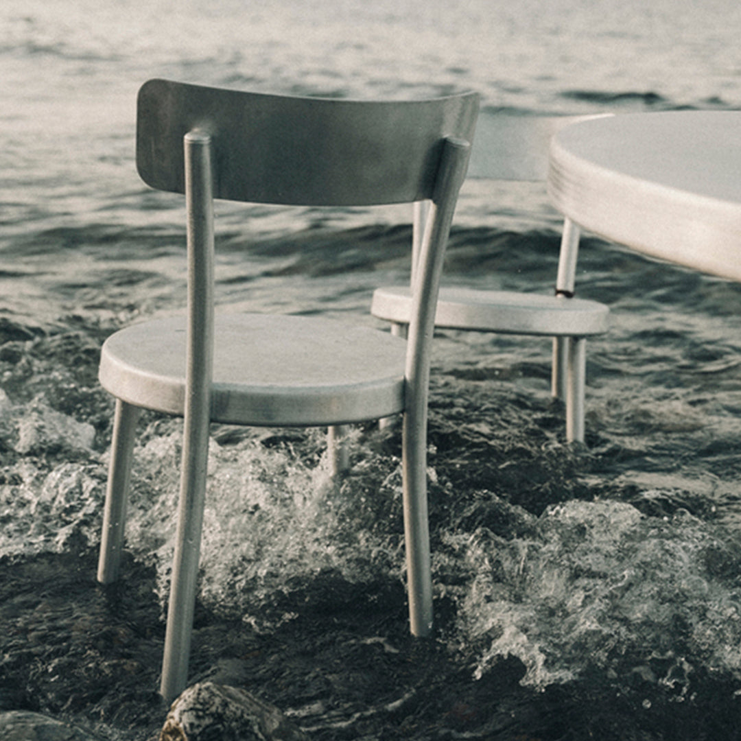 Silver metal chair with a minimalist design, featuring a smooth finish, set against a serene, watery background.