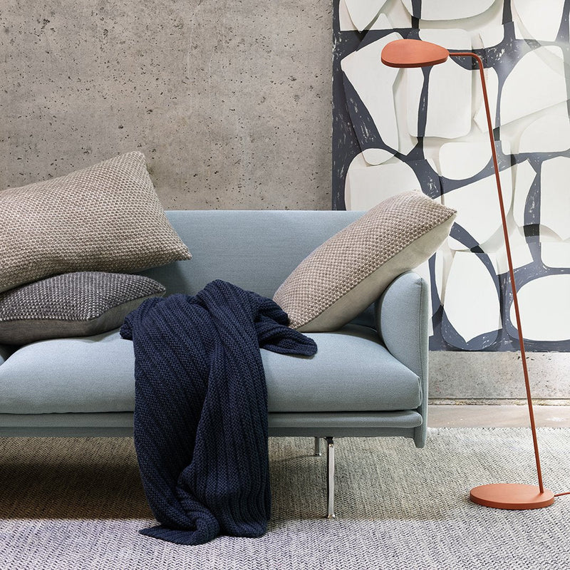 Light blue sofa with gray and navy pillows, navy throw blanket, and orange lamp against a textured, abstract wall.