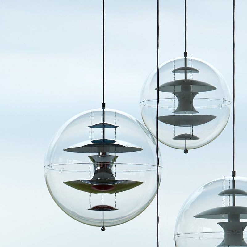 Transparent globe pendant lights with layered white and red patterns, hanging against a soft blue sky.