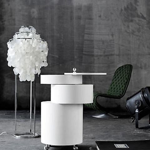 White circular side table with sleek layers, accompanied by a translucent white lamp and a green quilted chair.
