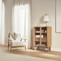 Light wood cabinet with woven shelves, complemented by a white upholstered chair and soft neutral tones throughout.