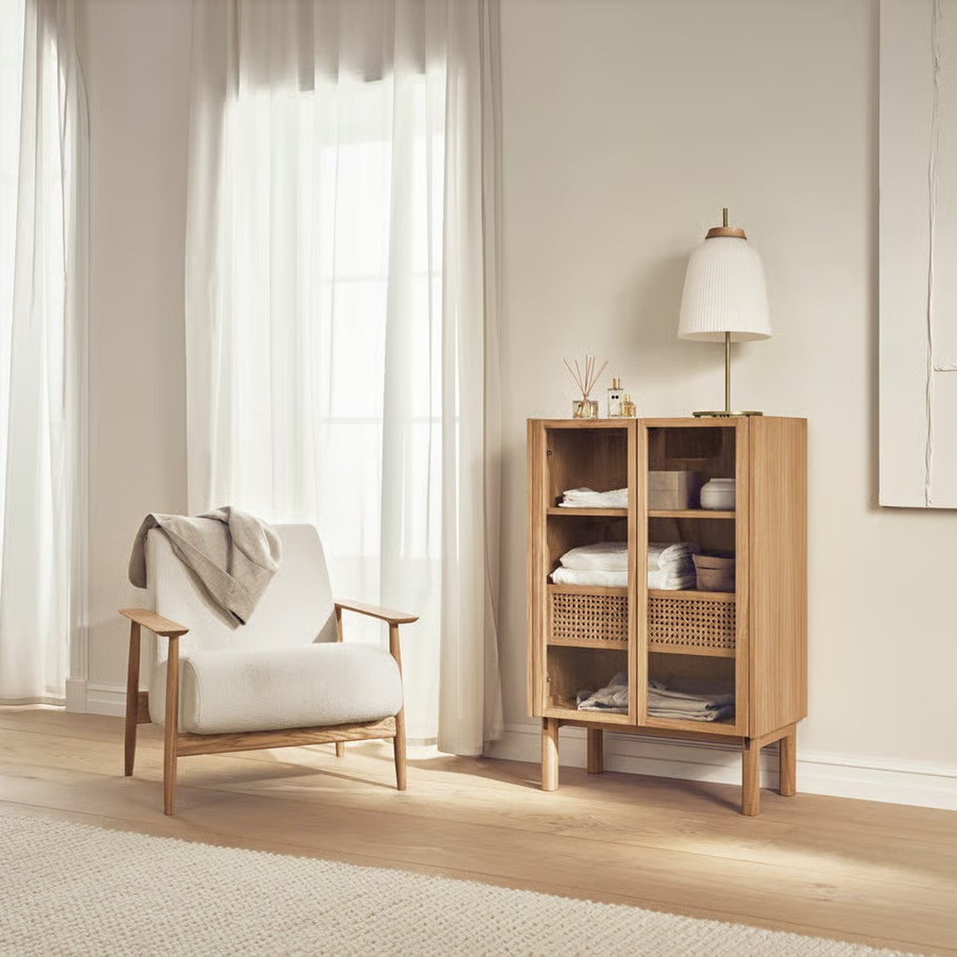 Light wood cabinet with woven rattan accents, paired with a neutral upholstered chair in a bright, airy room.