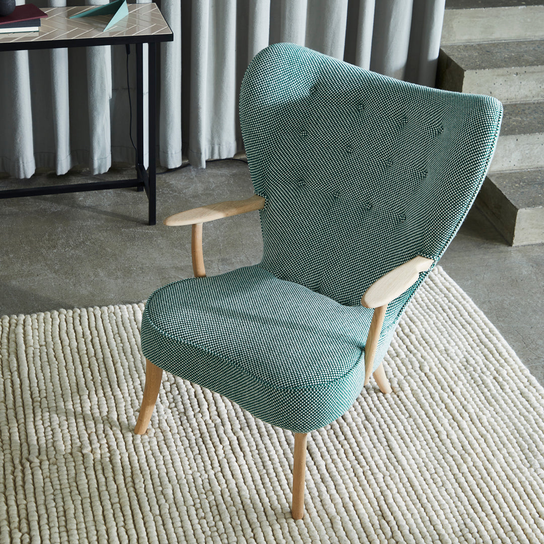 Aqua blue upholstered armchair with button-tufted detail and light wooden legs, set against a neutral rug.