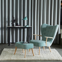 Aqua blue armchair with matching ottoman on a textured rug, complemented by gray curtains and a green lamp.