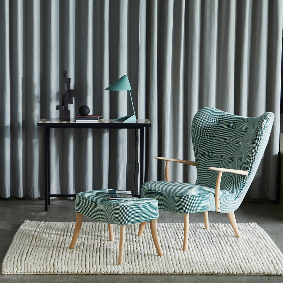 Aqua blue upholstered chair and ottoman on a textured rug against a backdrop of vertical gray curtains.