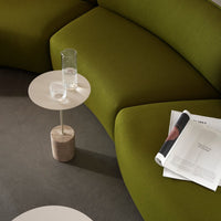 Green curved couch with smooth beige side table, showcasing modern, minimalist design and soft textures.