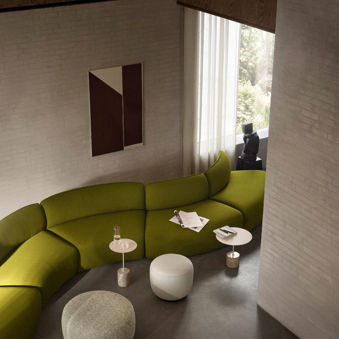 Curved green sofa in modern setting, complemented by white and light gray accent tables. Warm neutral walls and art.