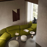Curved green sofa in modern setting, complemented by white and light gray accent tables. Warm neutral walls and art.