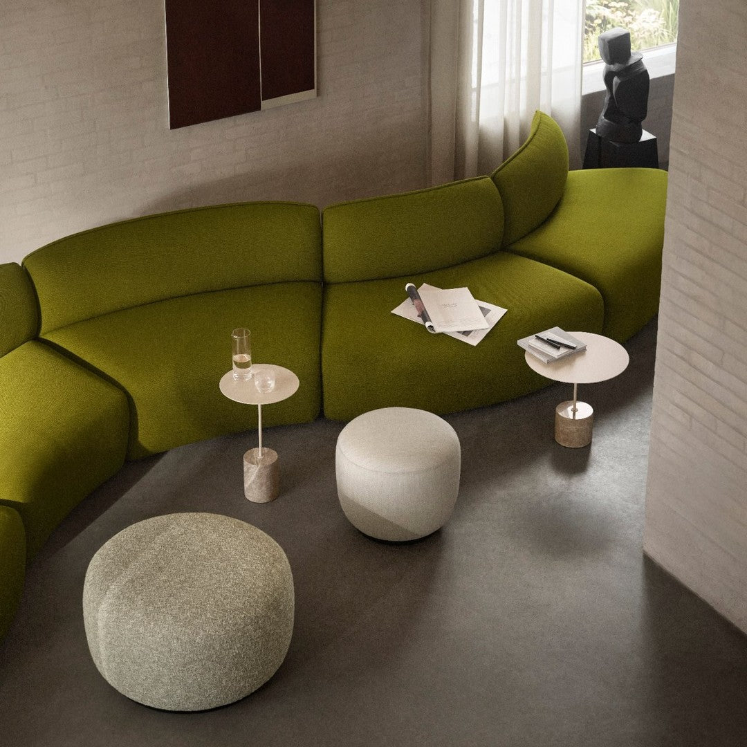 Curved sofa in olive green fabric with white and light gray accent tables on a smooth concrete floor.