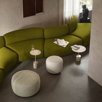 Curved sofa in olive green fabric with white and light gray accent tables on a smooth concrete floor.