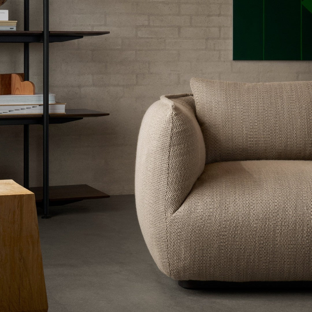 Beige textured fabric sofa with a rounded arm, set against a minimalist backdrop of earthy tones and neutral colors.