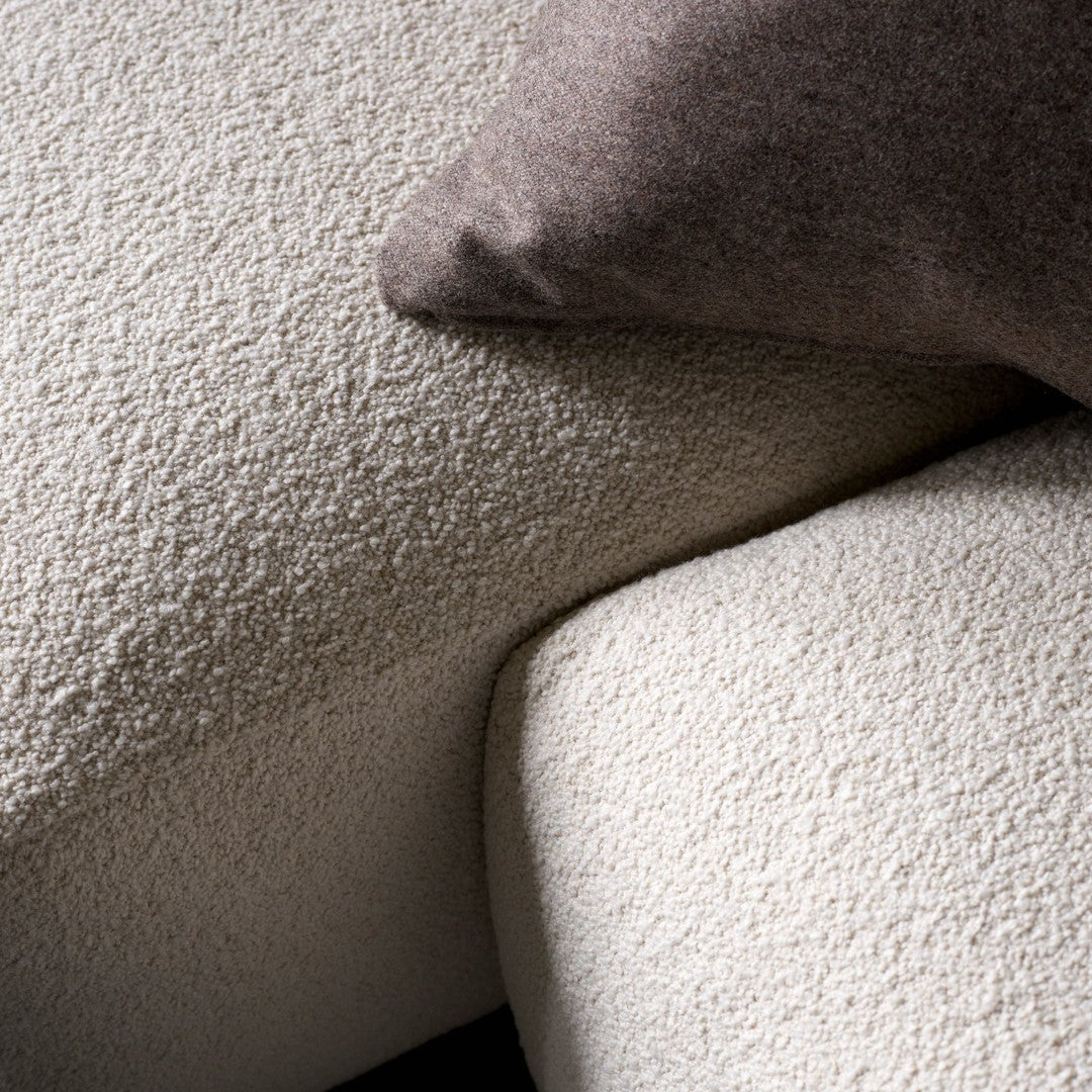 Textured cream and beige upholstery with a cozy brown accent pillow, featuring a soft, tactile surface.